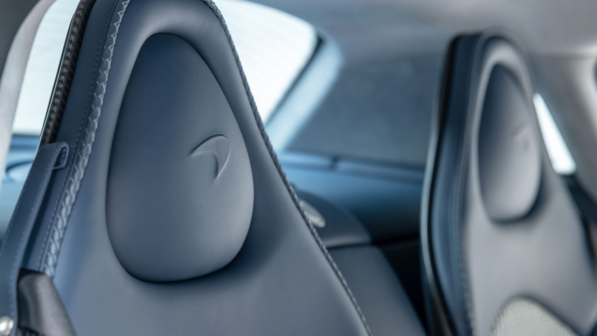 Close-up view of two black leather car seats with an embossed logo, featuring detailed stitching and a rear window in the background, from a 1962 Mercedes-Benz 300 SL Roadster offered at Broad Arrow Las Vegas 2025.