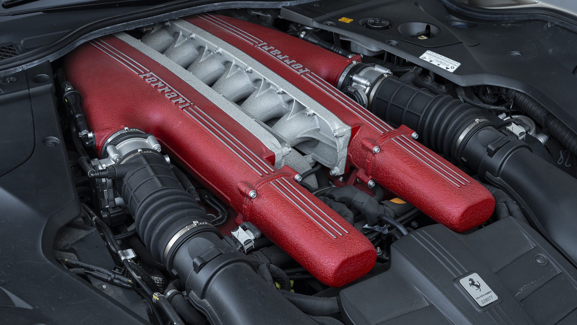 „Ferrari F12berlinetta“ variklio su raudonais įsiurbimo kolektoriais ir matomu „Ferrari“ prekės ženklu po automobilio gaubtu vaizdas iš arti, užfiksuotas „Broad Arrow Las Vegas“.