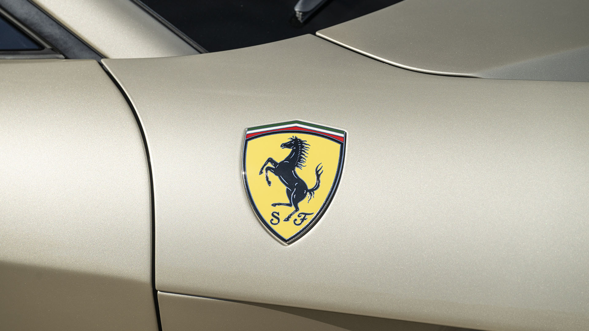 Iš arti geltono Ferrari logotipo su juodu svirduliuojančiu arkliu ant šviesaus aukso spalvos Ferrari F12berlinetta, 70-mečio leidimo, demonstruoto 2025 m. Broad Arrow Las Vegase, šoninis vaizdas.