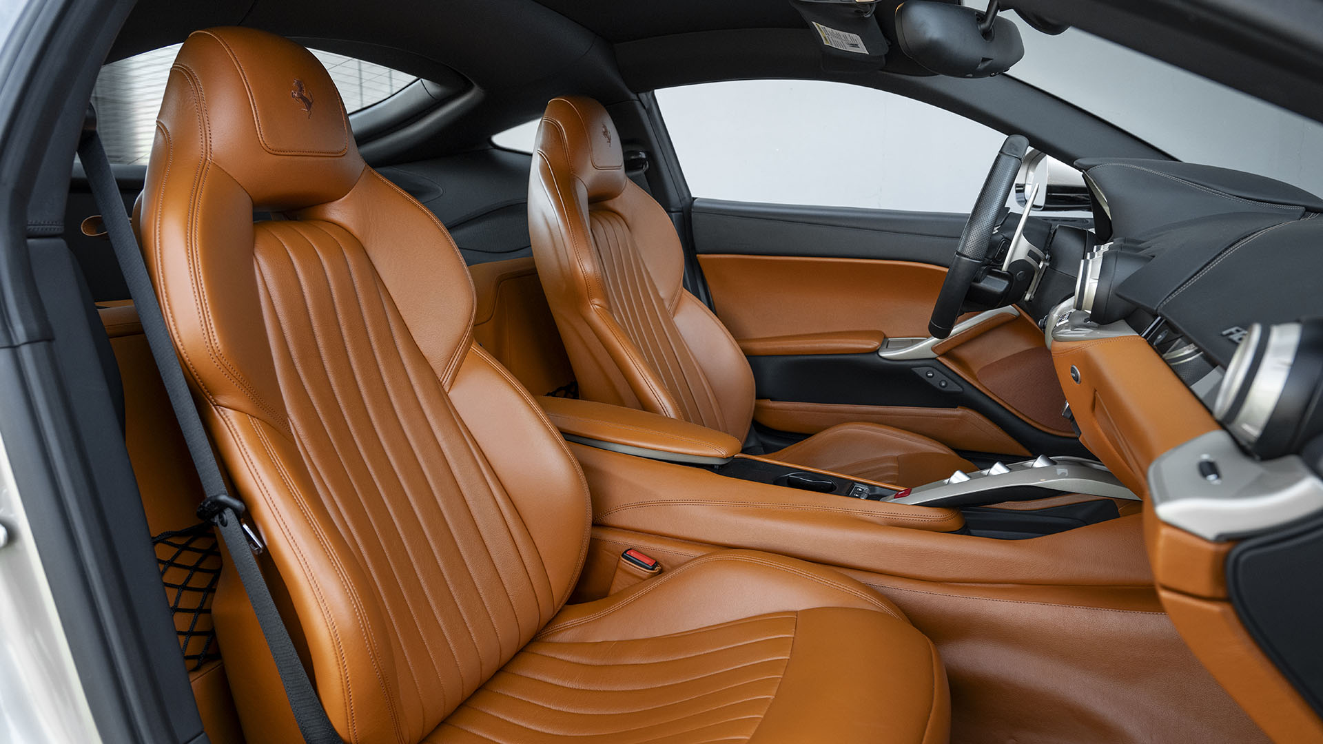 Ferrari F12berlinetta 70th Anniversary Edition interjeras su rusvos odos sėdynėmis, šiuolaikišku prietaisų skydeliu ir metaliniais apdailos akcentais – prabanga, demonstruojama 2025 m. Las Vegase.