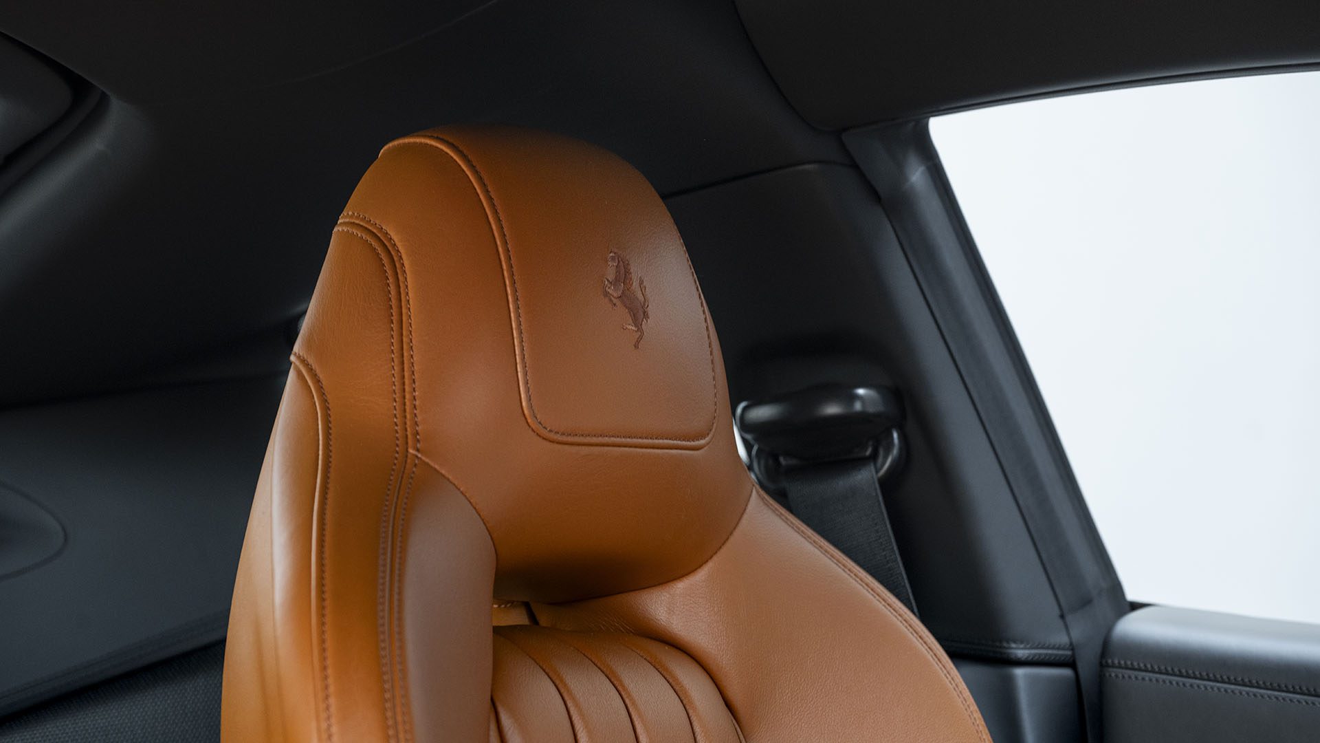 Iš arti gelsvos odinės automobilio sėdynės su įspaustu Ferrari logotipu, Ferrari F12berlinetta 70th Anniversary Edition viduje su juodos ir pilkos spalvos interjero detalėmis – puikiai tinka norint stilingai keliauti 2025 m. Las Vegase.