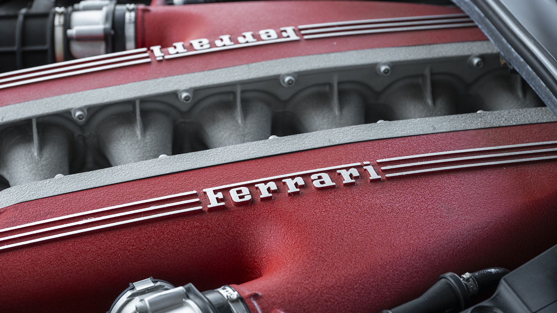 Raudono Ferrari F12berlinetta variklio gaubto vaizdas iš arti su aiškiai matomu Ferrari logotipu ir sidabriniais akcentais, fiksuojančiais jaudulį iki 2025 m. Las Vegaso.