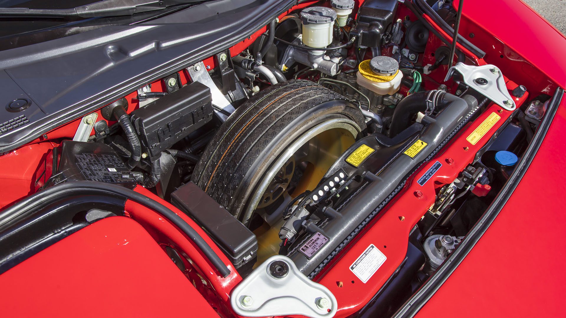 A spare tire is stored in the engine bay of a red 2022 Ferrari SF90 Spider, surrounded by various engine components and fluid reservoirs, a unique detail highlighted at the Broad Arrow Las Vegas 2025 Ferrari auction.