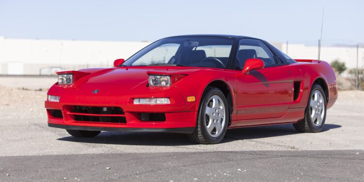 A red Ferrari SF90 Spider with pop-up headlights and silver wheels is parked on a paved surface outdoors under a clear sky, ready for Broad Arrow's Las Vegas 2025 event.