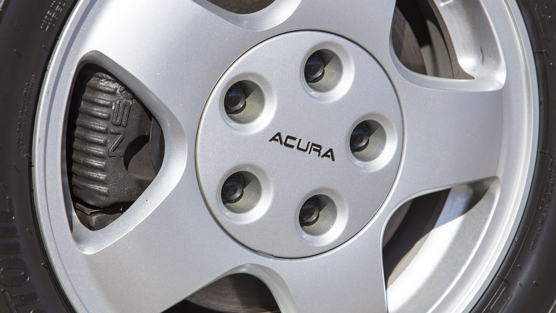 Close-up of a silver Acura car wheel with visible lug nuts and part of the brake caliper, reminiscent of the precision seen on a 2022 Ferrari SF90 Spider.
