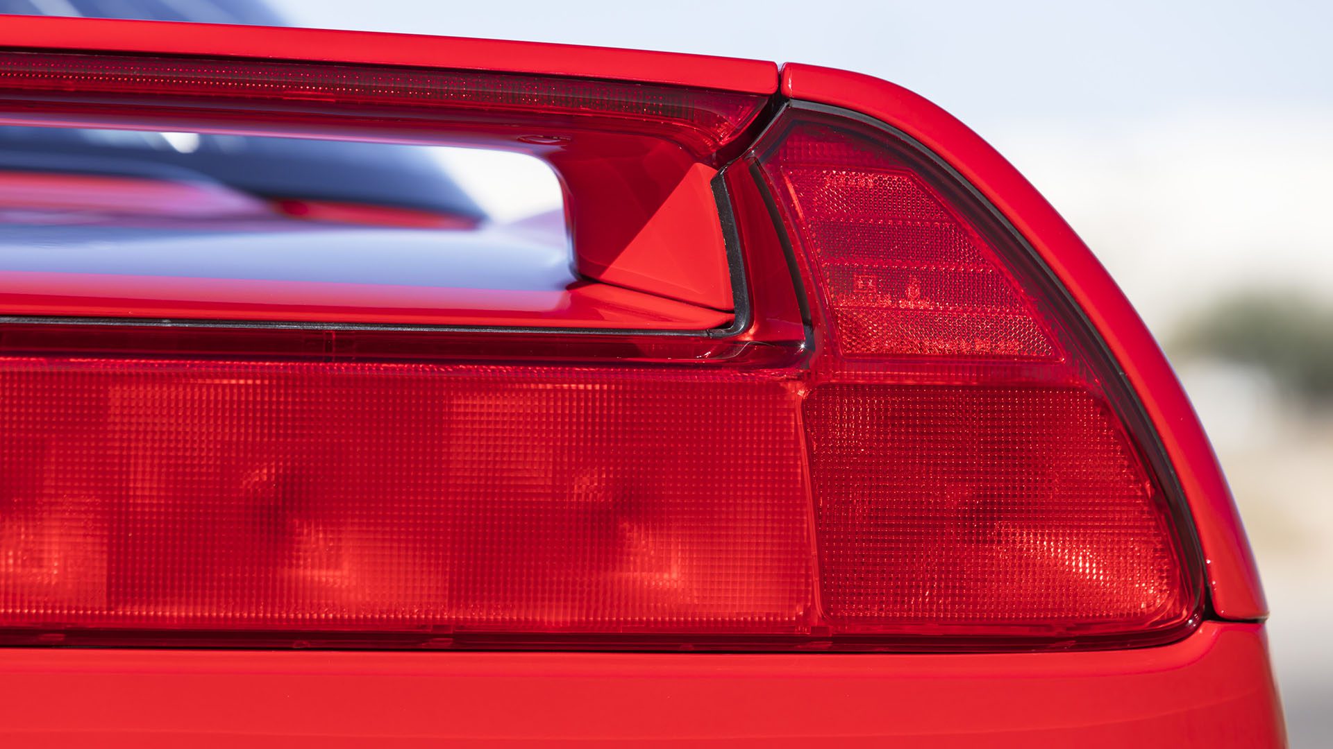 Close-up of a Ferrari SF90 Spider's rear taillight and spoiler, highlighting the angular design and smooth paint finish ahead of its 2025 Preview at Broad Arrow Las Vegas.