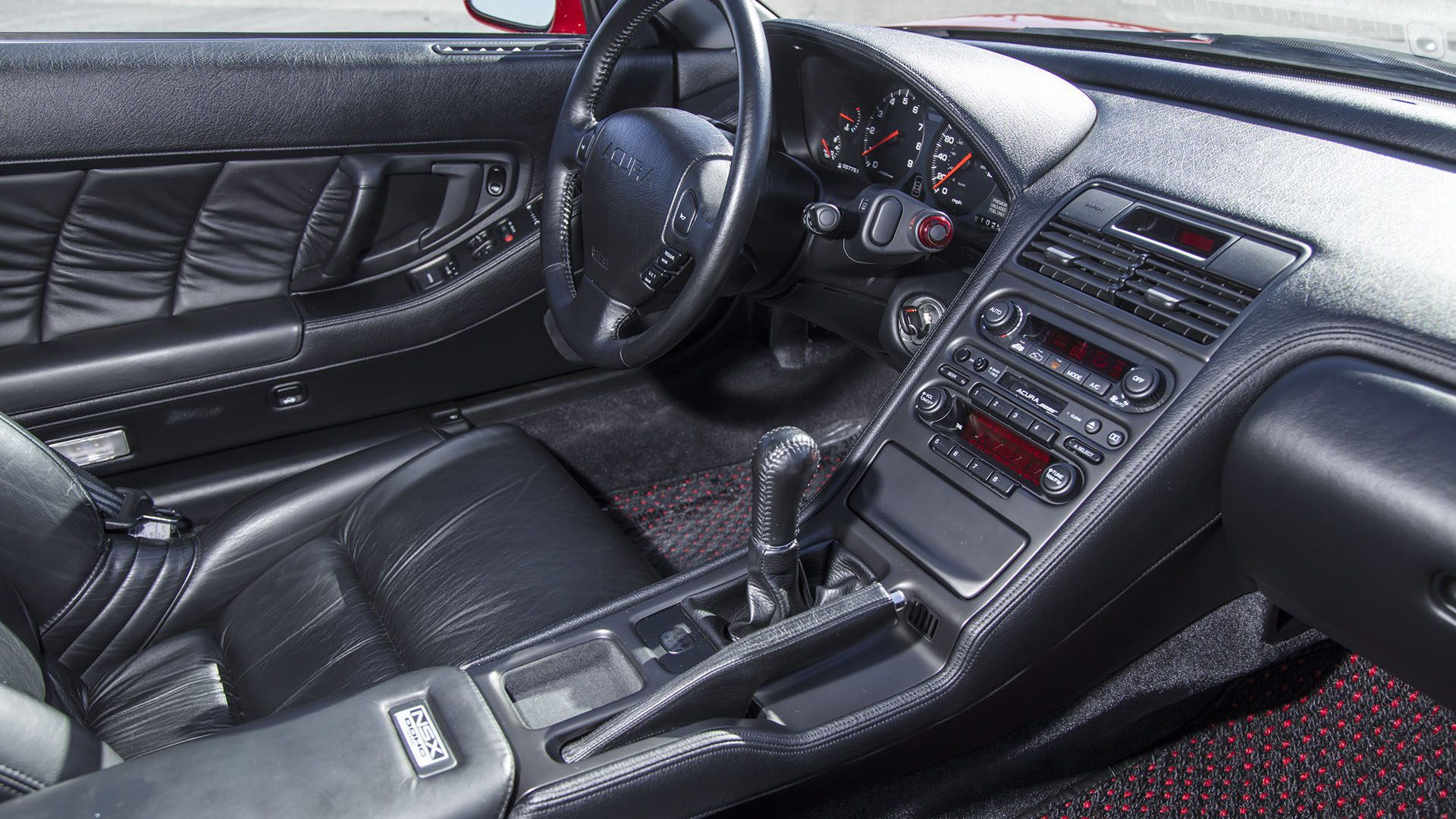 The black leather interior of this 2022 Ferrari SF90 Spider features a manual gear shift, analog gauges, and a center console with climate and audio controls—an exhilarating highlight at Broad Arrow Las Vegas 2025.