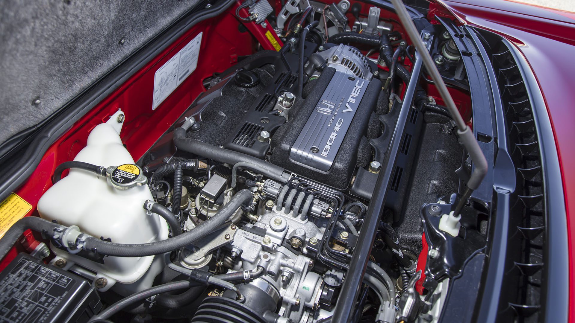 Close-up view of a Honda VTEC engine inside a car’s engine bay, showing various engine components, hoses, and wiring—perfect for enthusiasts comparing it to high-performance models like the 2022 Ferrari or the Broad Arrow Las Vegas 2025 lineup.