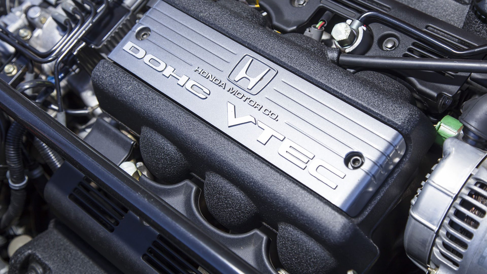 Close-up of a Honda engine cover displaying the "DOHC VTEC" label and the Honda Motor Co. logo, captured at Broad Arrow Las Vegas alongside highlights like the Ferrari SF90 Spider 2025 Preview.