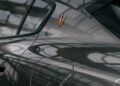 Close-up of a dark grey Maserati’s rear side panel featuring a gold trident emblem, with building reflections visible on the car’s glossy surface.
