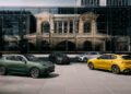 Four Maserati SUVs, including the Grecale Folgore with advanced EV tech, are parked in a modern plaza beside a glass building that beautifully reflects classical architecture.