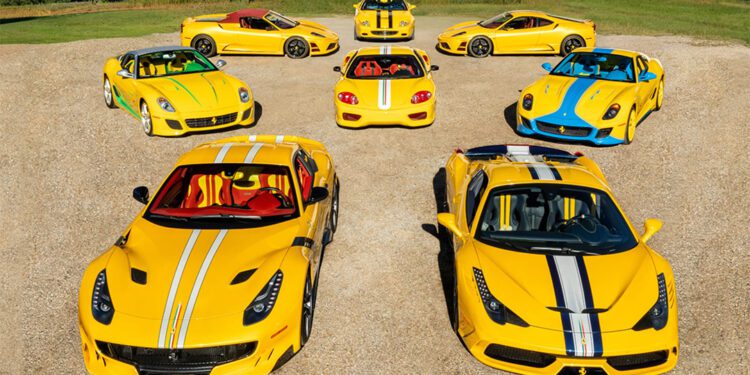 Eight yellow Ferrari sports cars with white and blue racing stripes, part of exclusive Ferrari Collections, are arranged in a semicircle on a gravel surface, with trees and grass in the background.
