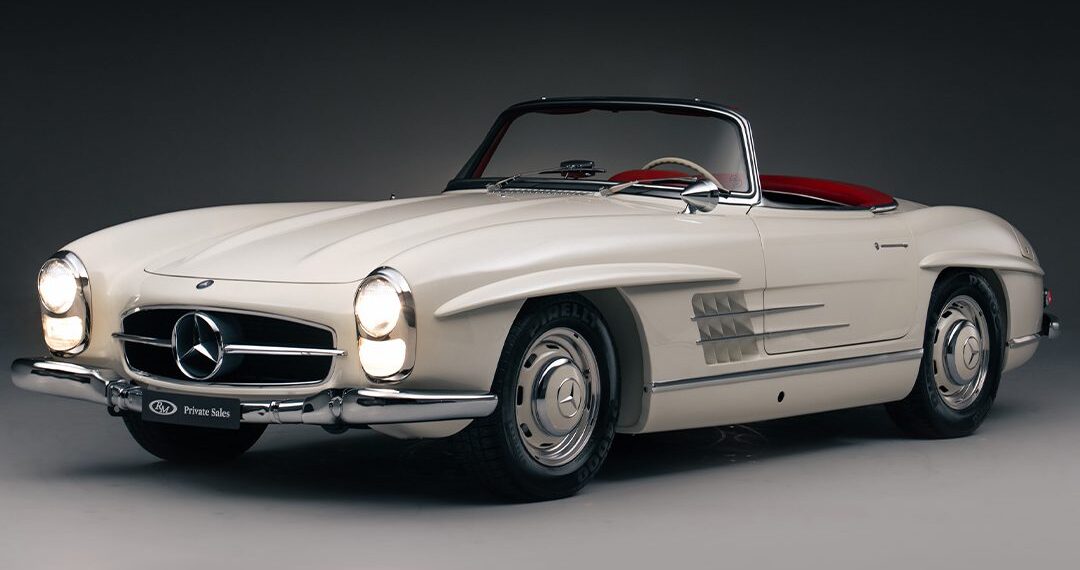 A white vintage Mercedes-Benz convertible with red interior, viewed from the front left side against a dark background—a true icon among classic cars.
