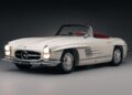 A white vintage Mercedes-Benz convertible with red interior, viewed from the front left side against a dark background—a true icon among classic cars.