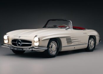 A white vintage Mercedes-Benz convertible with red interior, viewed from the front left side against a dark background—a true icon among classic cars.