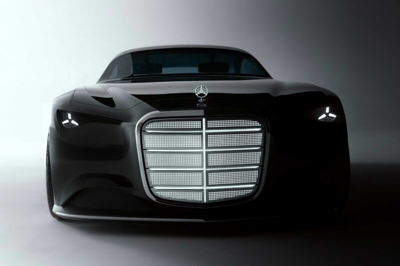 Front view of the Mercedes-Benz Vision Iconic revives classic elegance for the digital era, showcasing a sleek black concept car with a large illuminated grille and minimalist headlights against a gradient grey background.