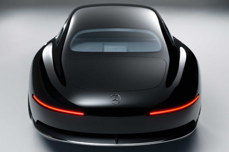 A sleek black Mercedes-Benz Vision Iconic concept car is shown from the rear, featuring smooth curves and a continuous red taillight that revives classic elegance for the digital era.