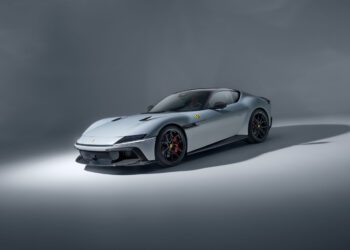 A silver Ferrari sports car is parked on a plain, light-gray studio background, shown from a front three-quarter angle.