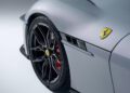Close-up of a silver Ferrari 12Cilindri sports car showing the front left wheel, tire, Ferrari logo, brake caliper, and part of the hood and fender vent with bespoke NOVITEC customizations.