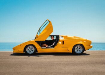 A man sits in a yellow Lamborghini with the doors open, exuding style reminiscent of the Miami Beach Collection.