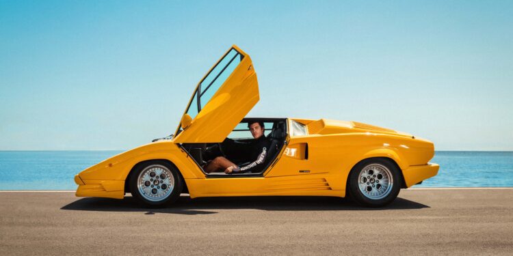 A man sits in a yellow Lamborghini with the doors open, exuding style reminiscent of the Miami Beach Collection.