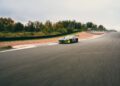A Mercedes AMG TRACK SPORT race car speeds along a paved racetrack, surrounded by trees and greenery under a cloudy sky, capturing the essence of racing concept.
