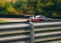 A camouflaged Mercedes speeds on a race track behind a metal barrier, with blurred greenery in the background, showcasing the thrill of CONCEPT AMG TRACK SPORT on modern circuits.