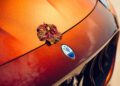 A single leaf rests on the hood of an orange Maserati Grecale Tributo with the car’s emblem visible in the center.