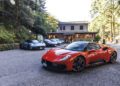 A red Maserati sports car is parked in front of a building, with several other sports cars and trees in the background, offering an authentic taste of the MCPURA Driving Experience inspired by Italy.