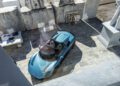 A blue Maserati convertible sports car is parked in a stone courtyard in Italy, surrounded by large marble blocks and a statue of a person.