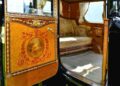 The interior of an ornate vintage carriage with elaborate woodwork, floral upholstery, and decorative painted details on the door evokes the bespoke luxury found in a classic Rolls-Royce Phantom.