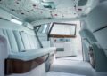 The image shows the luxurious interior of a Bespoke Rolls-Royce with light blue seats, wood trim, and a floral-patterned ceiling. The rear door is open, revealing matching interior details, celebrating 100 Years of Rolls-Royce Phantoms craftsmanship.