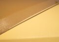 Close-up of two metallic car panels, one beige and one yellow, separated by a narrow gap and covered in fine glitter-like particles—an ode to Bespoke Rolls-Royce craftsmanship.