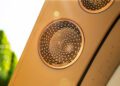 Close-up of a circular Bespoke Rolls-Royce Audio speaker with a metallic grille, mounted on a tan colored interior panel of the Rolls-Royce Spectre.