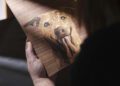A person holds a wooden plaque featuring an engraved image of a dog with a stick in its mouth, illuminated by a beam of light—a true symbol of dog dedication, much like bespoke Rolls-Royce craftsmanship.
