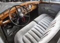 Vintage car interior with a bespoke wooden dashboard, large black steering wheel, analog gauges, and gray upholstered seats—evoking the timeless luxury of classic Rolls-Royce Phantoms.