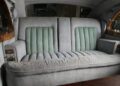 Vintage car interior featuring a bespoke wide, light gray upholstered backseat with green vertical cushions, wood trim, and control panels on the side armrests—evoking the luxury of classic Rolls-Royce Phantoms.