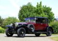 A vintage maroon and black Rolls-Royce Phantom is parked on a paved driveway, surrounded by trees and greenery—a bespoke classic amidst nature.