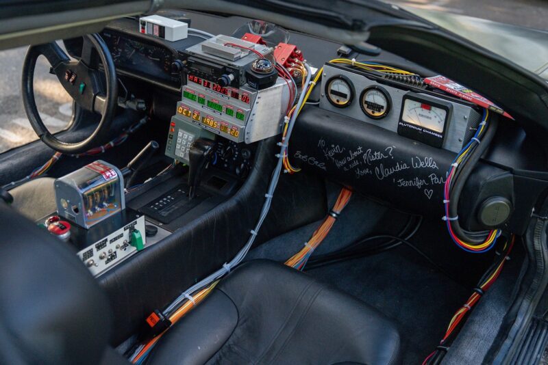 Interior of a car with retro-futuristic control panels, gauges, switches, colorful wiring, and handwritten signatures on the dashboard—a true Outatime vibe perfect for any Film Friday or Petrolicious feature.