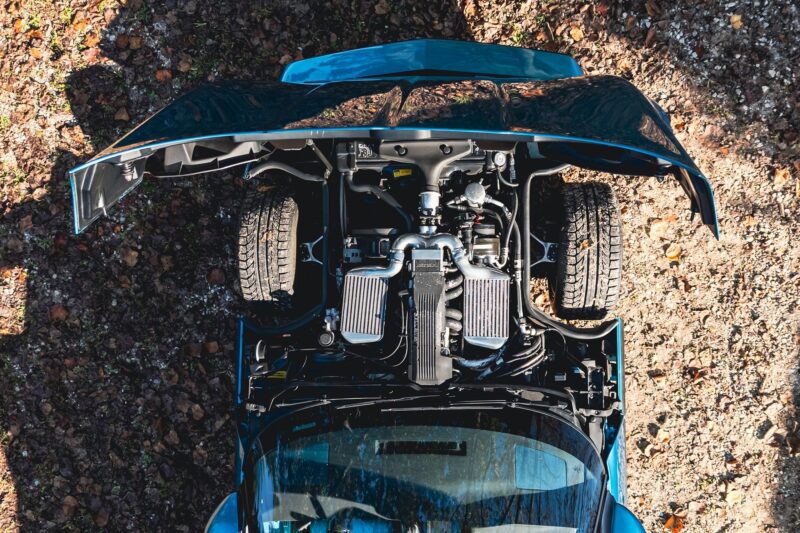 Aerial view of a blue Callaway Corvette with its hood open, exposing the engine and front tires, parked on leaf- and dirt-covered ground—a true Petrolicious moment worthy of Film Friday.