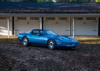 A blue Callaway Corvette, worthy of a Petrolicious Film Friday feature, is parked on a gravel surface in front of a row of white garage doors.