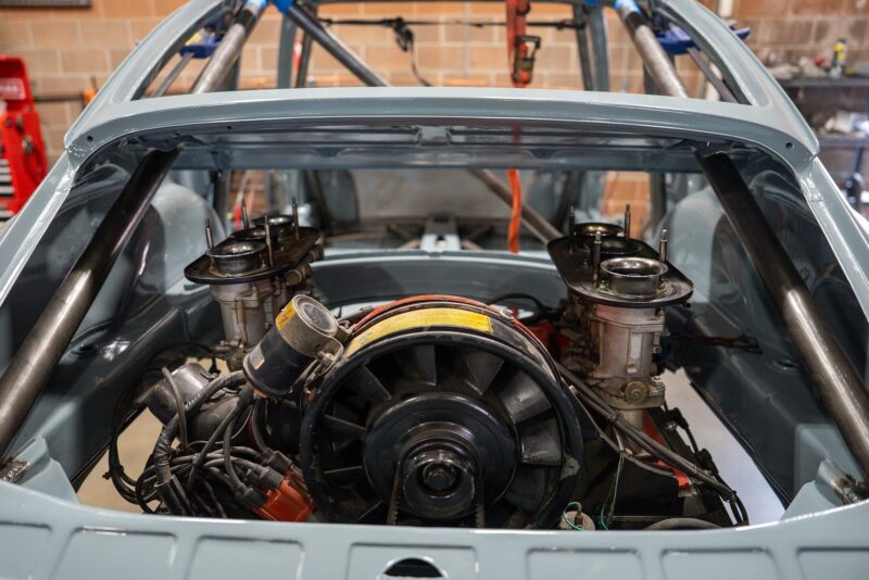Rear view of a classic car chassis revealing an exposed air-cooled engine and roll cage in a garage, reminiscent of a Petrolicious feature.