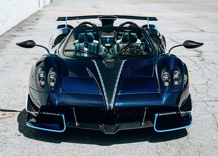 Front view of a dark blue Pagani Huayra Roadster with visible carbon fiber detailing, parked on concrete—this 864HP supercar is showcased by O'Gara Coach.