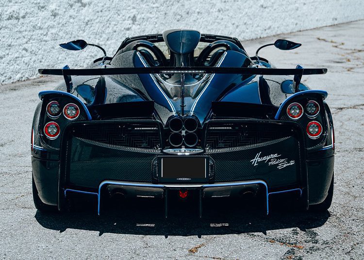 Rear view of a black Pagani Huayra Roadster 1-of-1 parked on pavement, showcasing visible carbon fiber, taillights, spoiler, and "Huayra" badge—an exclusive masterpiece from O'Gara Coach.