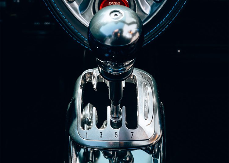 Close-up view of a manual car gear shift lever with a metallic finish, showing gear positions 1 through 7 and reverse, set against a black background—perfect for the 864HP Pagani Huayra Roadster featured at O'Gara Coach.