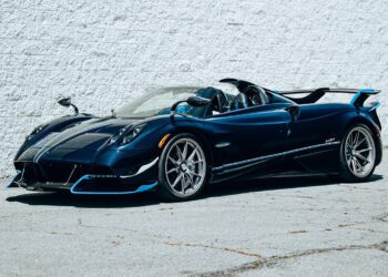 A blue Pagani Huayra Roadster manual supercar is parked on a concrete surface next to a white brick wall.