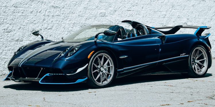 A blue Pagani Huayra Roadster manual supercar is parked on a concrete surface next to a white brick wall.