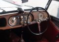 Close-up of a Morgan Plus Four dashboard featuring analog gauges, a wooden panel, round steering wheel, and manual gear levers—celebrating the 75th Anniversary with timeless craftsmanship.