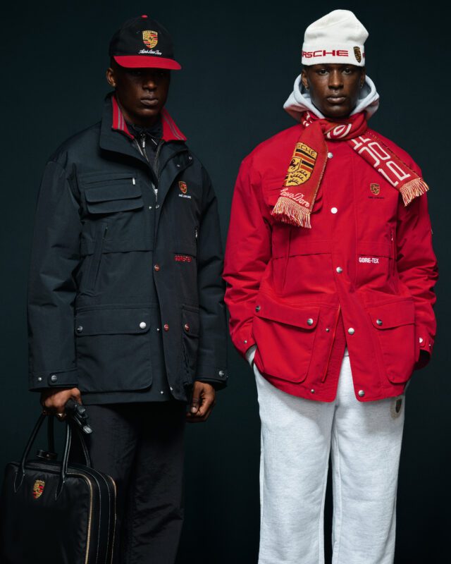 Du žmonės su Aimé Leon Dore x Porsche striukėmis, skrybėlėmis ir aksesuarais pozuoja tamsiame fone – vienas juodas su portfeliu, kitas raudonas su skara ir baltomis kelnėmis iš 2025 m. rudens/žiemos kolekcijos.