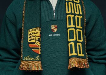 Person wearing a green sweater with a Porsche crest and "Aimé Leon Dore" logo, accessorized with a black and yellow Porsche scarf, showcasing the refined style of the 2025 Fall/Winter Collection.